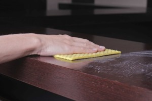 Close up of hand cleaning wooden table with furniture polish. Using yellow sponge for cleaning dusty wood. House cleaning and home hygiene concept